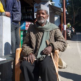 An old man sitting on a chair outside a shop in the mountains