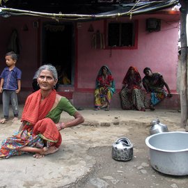 Woman sitting in front of home with three people and a child in the background