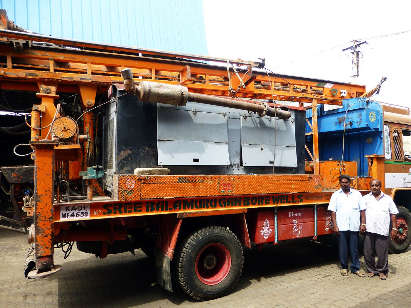 Two men standing in front of borewell digging rig