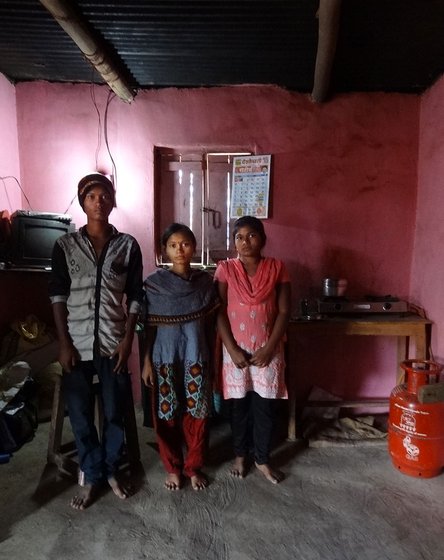 A young boy and two young girls, all sblings, stand in their house