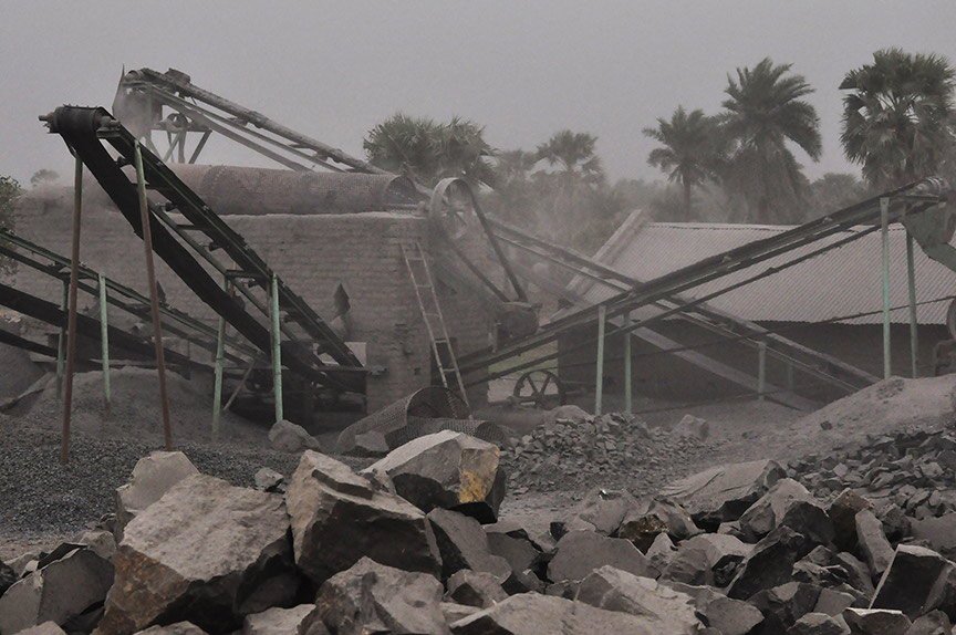 Close-up of a crusher, featuring conveyor belts that carry the rocks to a central piston, which breaks them. Labourers have to pile the rocks onto the belts; they can and do get caught in the belts and crushed themselves