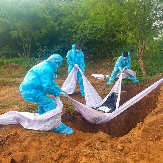 The volunteers lower a body into a pit eight feet deep, cover up the pit and pour a disinfectant powder across the grave

