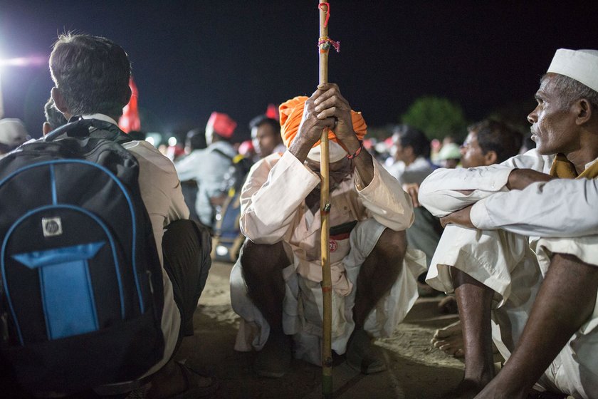 An old man sitting on his haunches leaning his head against his staff