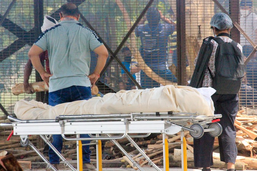 Left: The dead body of a Covid-positive patient resting on a stretcher in the crematorium premises. Right: A body burning on an open pyre at Nigam Bodh Ghat