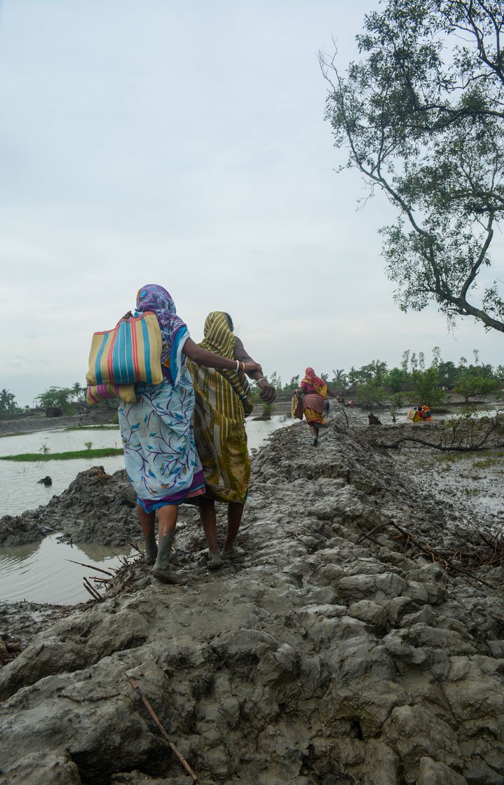 Left: Women of Kalidaspur village, Chhoto Molla Khali island, Gosaba block, returning home after collecting relief items from a local organisation. Right: Children playing during the high tide in Baliara village on Mousuni island. Their fathers work as a migrant labourers in the paddy fields of Uttarakhand.

