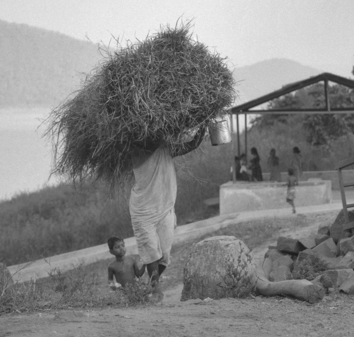 Woman with load of firewood on head being accompanied by child 